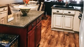Una cocina con armarios de madera, encimera de granito y un comedor con sillas blancas.