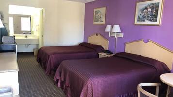 Habitación de hotel con dos camas, un escritorio, una silla, una lámpara y un cuadro en la pared.