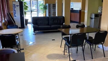 Un hall de hotel con un sofá, una mesa de comedor con sillas, un refrigerador y una cafetera.