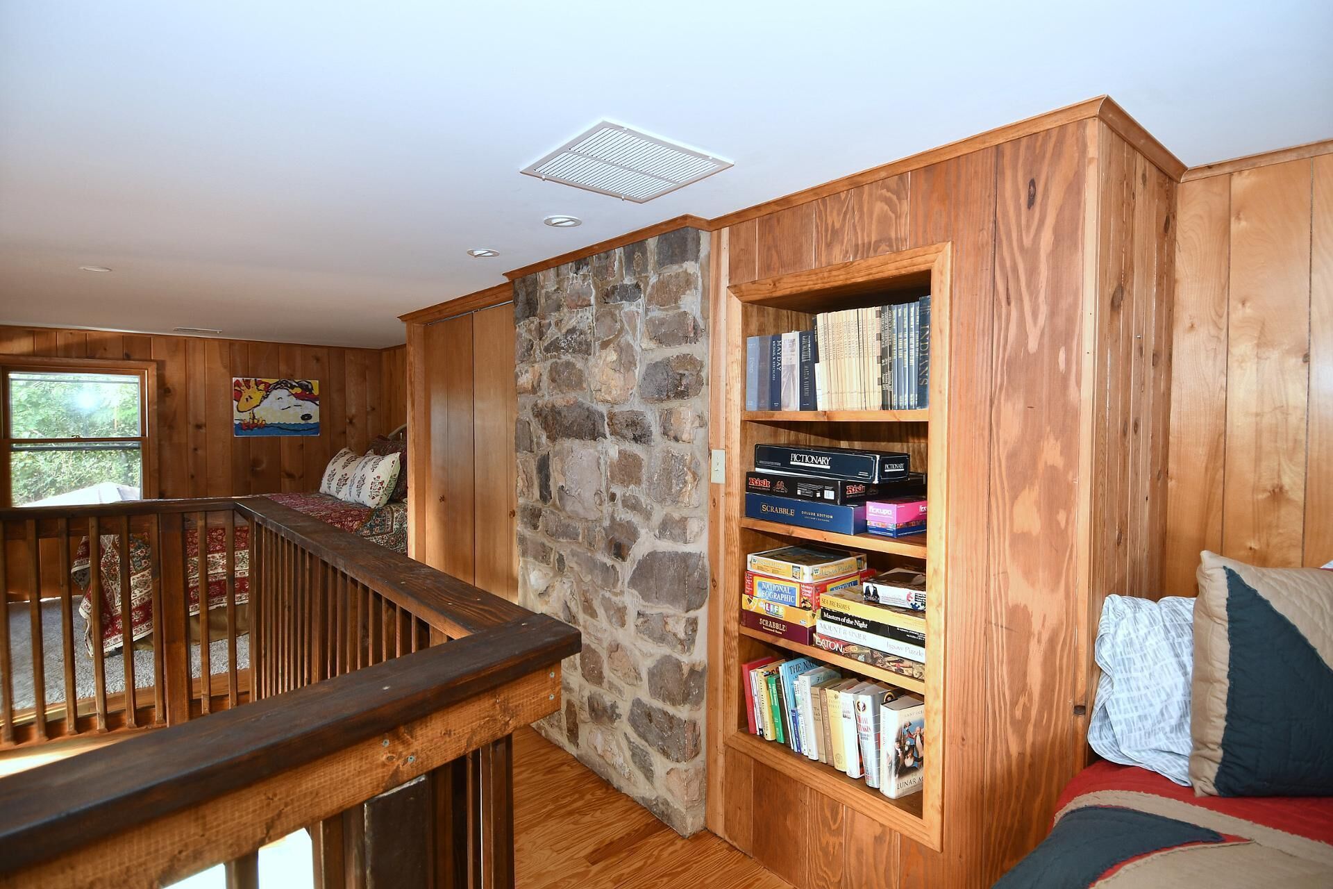 Un coin lecture chaleureux avec un mur en pierre, des étagères en bois remplies de livres et un espace détente confortable avec des coussins.
