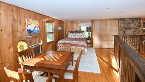 Ein Holzinterieur mit einem Bett, einem Esstisch mit Stühlen, einem Bücherregal und einer Steinwand.