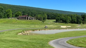 Un campo de golf con un club house, un estanque y una colina boscosa al fondo.