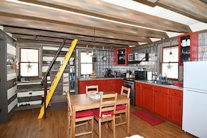 Cocina compacta con armarios rojos, una mesa de comedor de madera y una escalera que sube a un nivel superior.