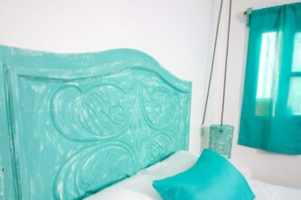 A bed with a turquoise headboard, white bedding, and a teal pillow.