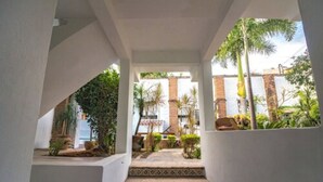 A covered outdoor staircase leading to a building with a brick wall and a view of a palm tree and greenery. - Hotel Costa 55 (Puerto Escondido)