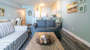 A living room with a striped sofa, a blue sofa, and a coffee table with decorative items. - Spacious 9th floor, 2 bedroom plus bunkroom with STUNNING OCEAN & POOL VIEWS! (Panama City Beach)