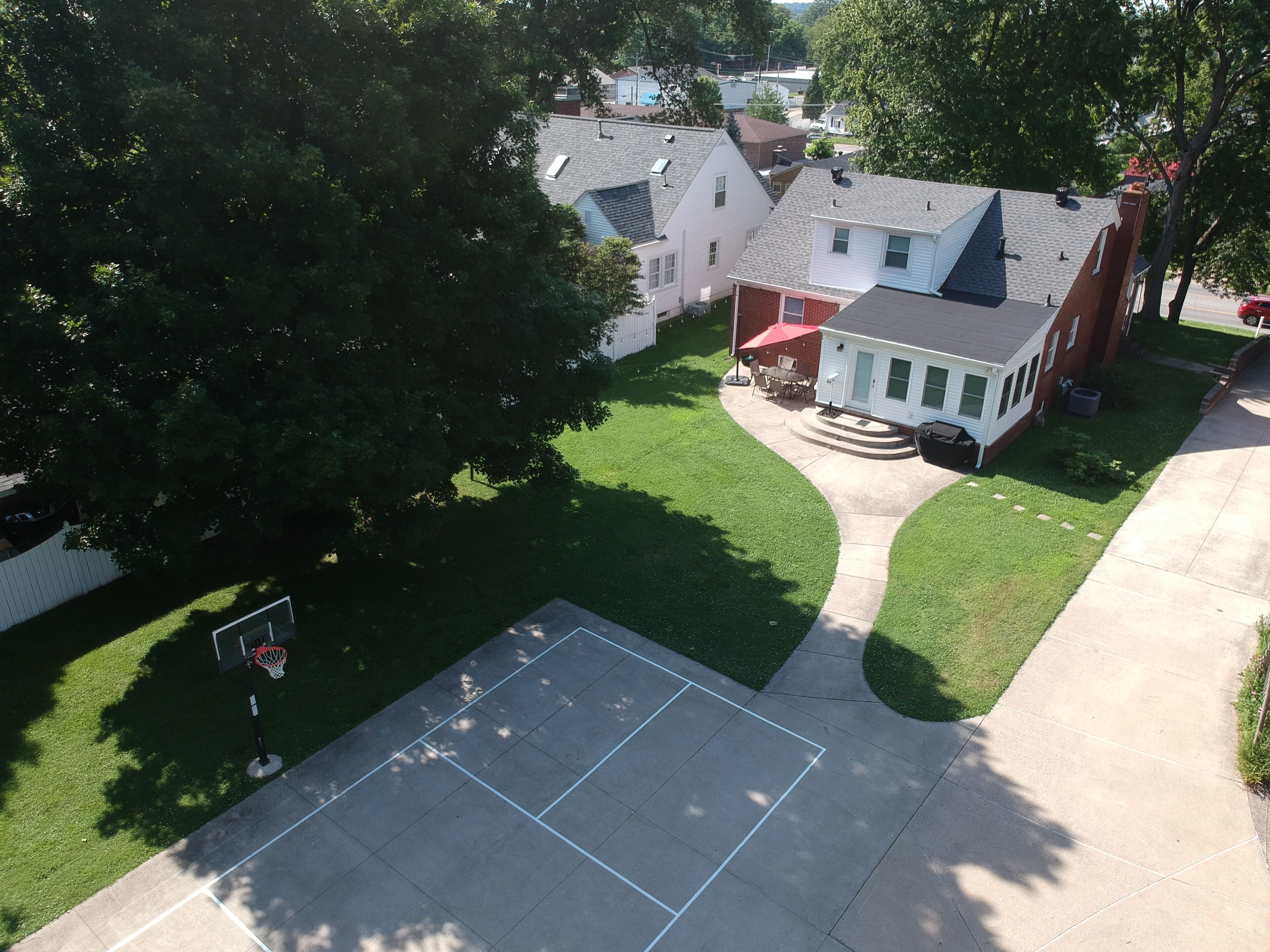 A residential area with a basketball court, houses, and a large tree.