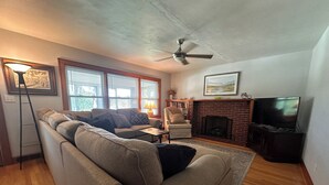 A living room with a sofa, armchair, fireplace, TV, and a ceiling fan.