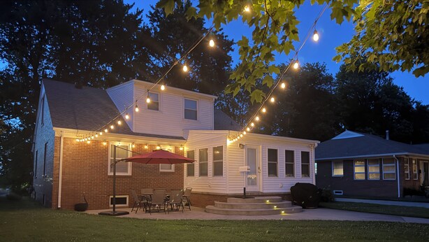 A house with a patio, string lights, and a red umbrella.