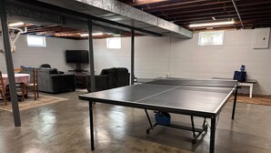 A ping pong table in a spacious room with a concrete floor, a sofa, and a television in the background.