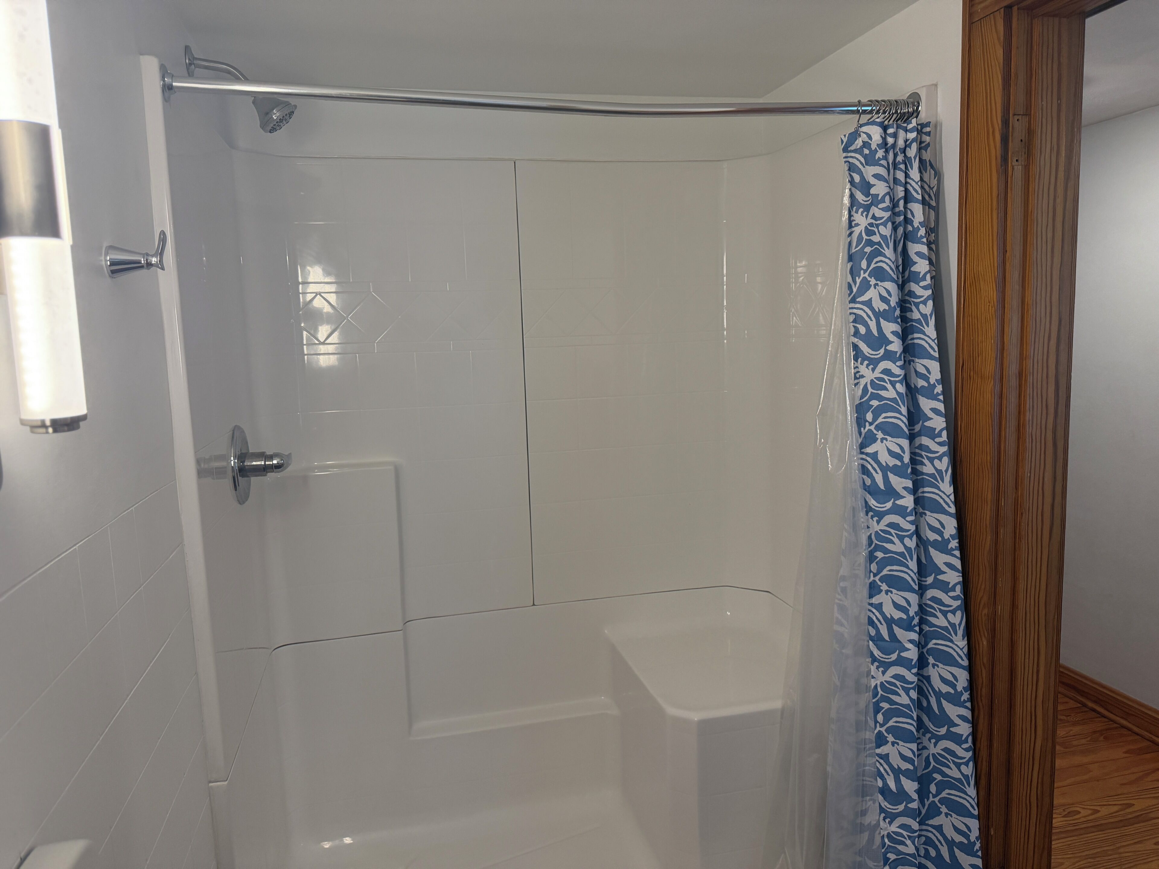 A shower area with a glass door, a showerhead, and a blue patterned shower curtain.