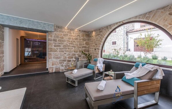 A modern lounge area with stone walls, two sofas, a small table, and a large arched window offering a view of the outdoors.