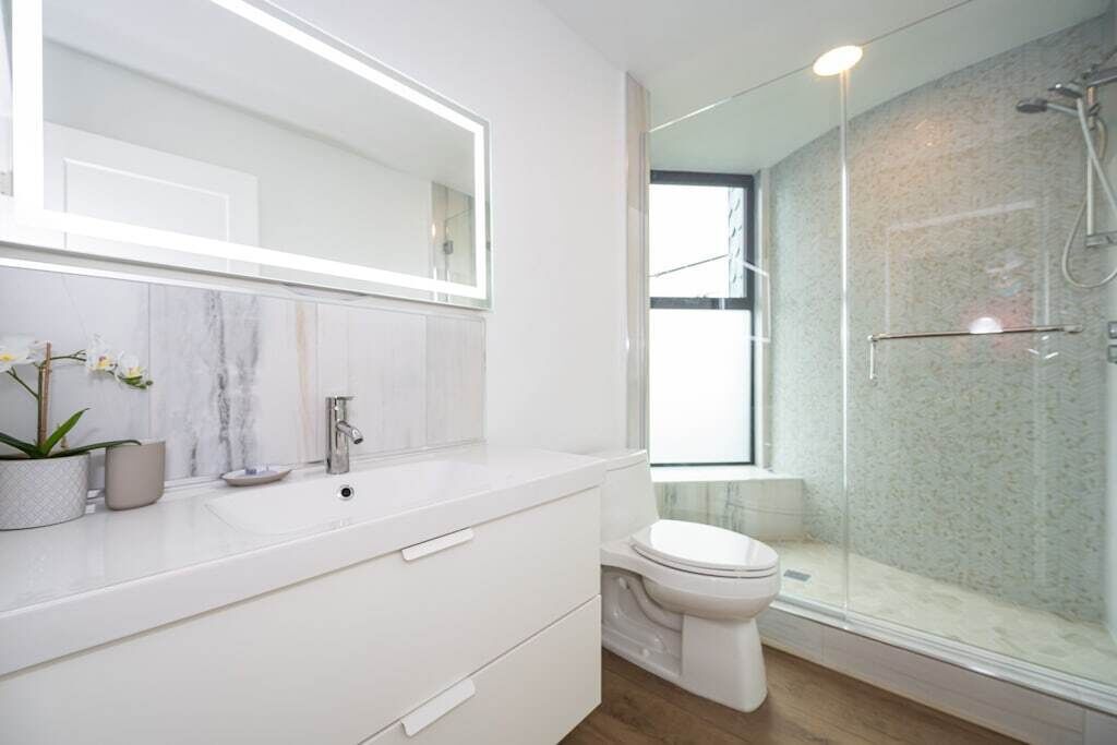 Une salle de bain moderne avec un grand miroir, un lavabo blanc, des toilettes et une douche séparée par une paroi de verre.