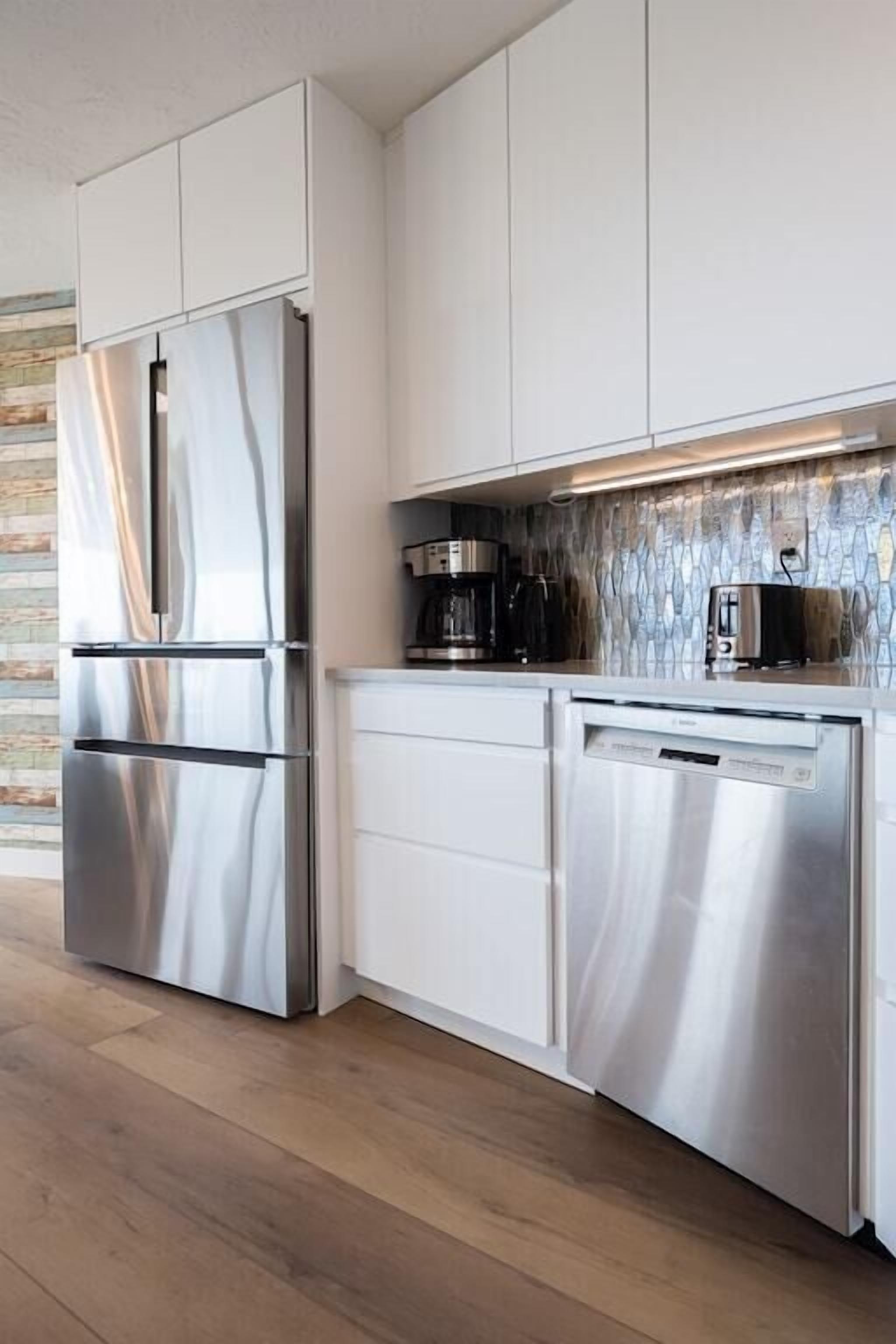 A modern kitchen with stainless steel appliances, white cabinetry, and a backsplash with a geometric pattern.