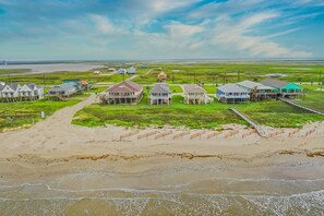 A coastal area with houses on stilts, a sandy beach, and a view of the ocean.