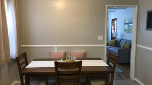 Zona pranzo con tavolo e sedie in legno, una ventola a soffitto e vista sul soggiorno.