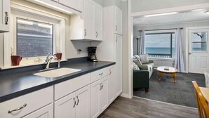 Une cuisine avec des meubles blancs, un plan de travail noir et une fenêtre donnant sur la mer.