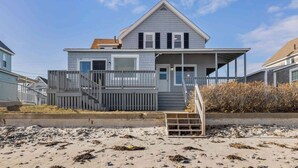 Une maison de plage à deux étages, dotée d’un balcon, d’une véranda et d’un escalier menant à l’entrée.