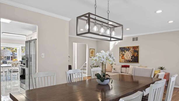 A dining area with a wooden table, white chairs, a modern chandelier, and a painting on the wall. - 5 bedrooms with 4 Full Bath, Fire Pit,  BBQ and Plush Amen on 1/2 acre (Silver Spring)