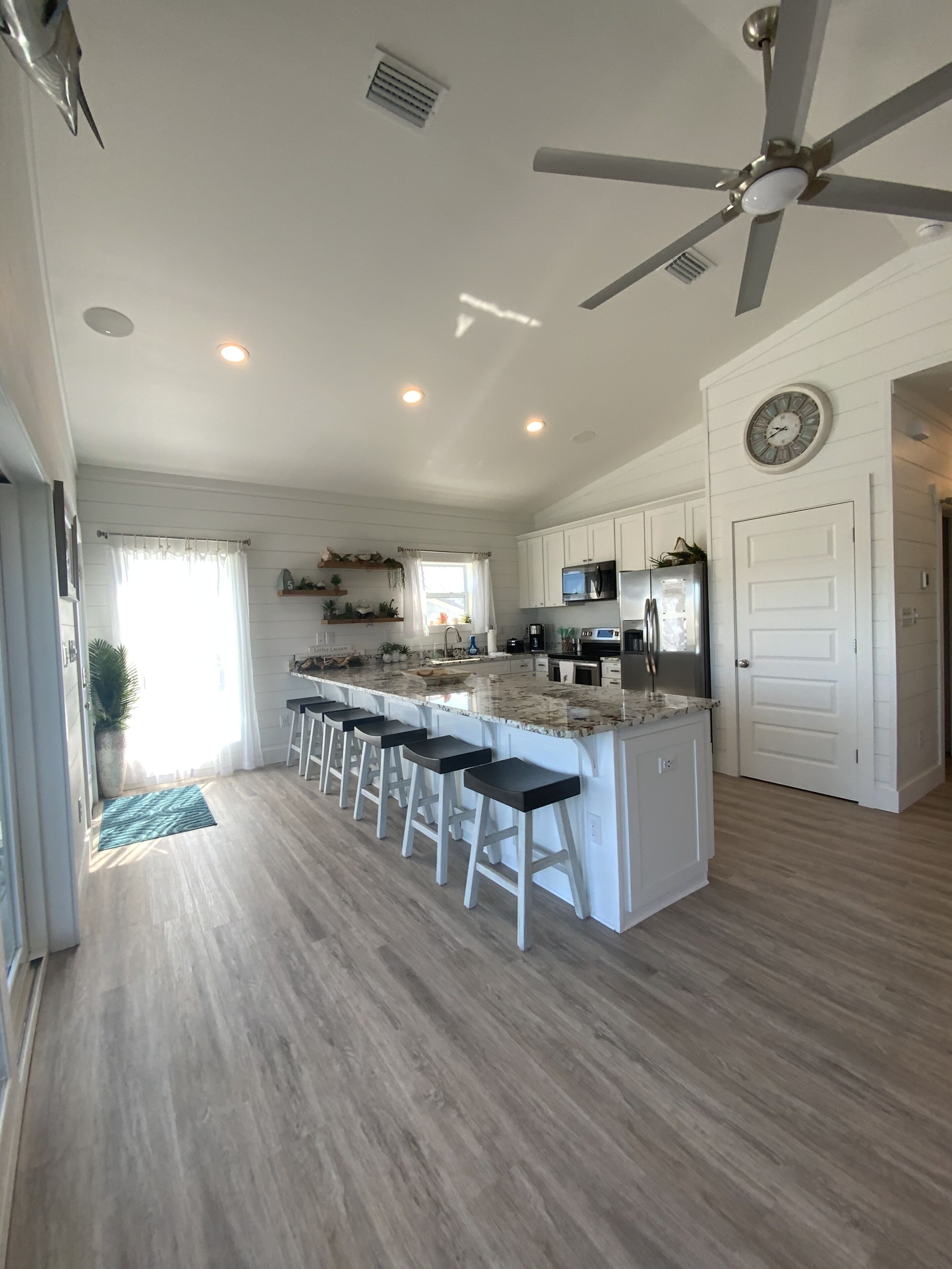 A modern kitchen with a central island, bar stools, a ceiling fan, and a clock on the wall.