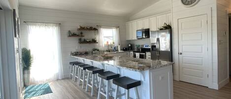 A modern kitchen with a central island, bar stools, a ceiling fan, and a clock on the wall.