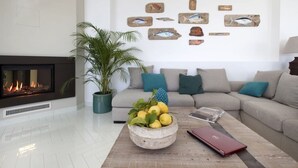 A modern living room with a fireplace, a sofa set, a coffee table with fruits, and wall art of fish.