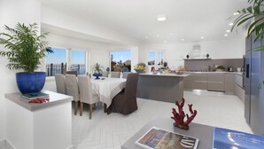 A modern kitchen with a central island, a dining area with a table and chairs, and a view of the sea.