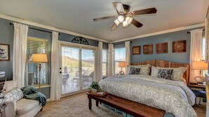 A bedroom with a large bed, a ceiling fan, a bench, and a view of the outdoors through the windows. - The Retreat at Thumb Butte (Prescott)