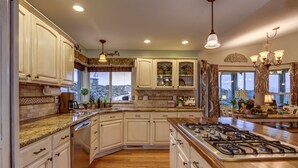 A spacious kitchen with white cabinetry, granite countertops, a central island with a stove, and a large window offering a scenic view. - The Retreat at Thumb Butte (Prescott)