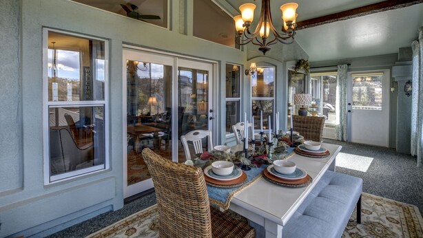 A dining area with a large table set for six, surrounded by wicker chairs, and a chandelier above. - The Retreat at Thumb Butte (Prescott)