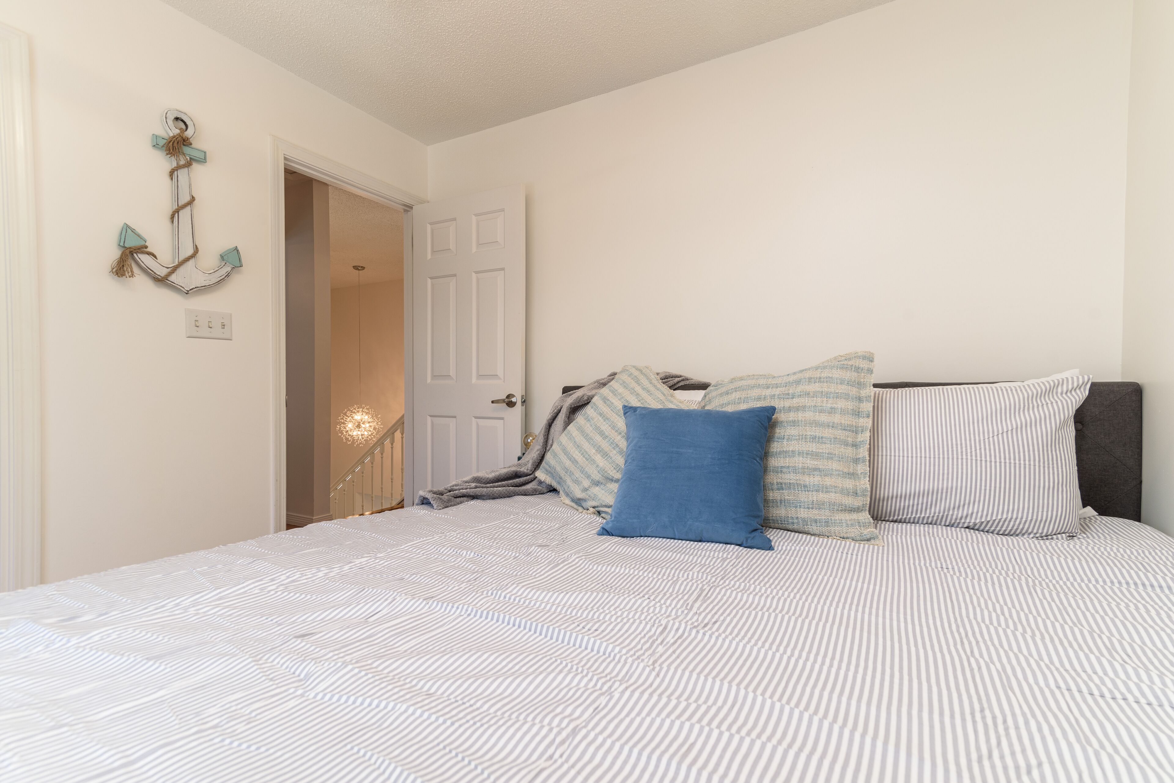 A bedroom with a bed, pillows, a wall anchor decoration, and a door leading to another room.