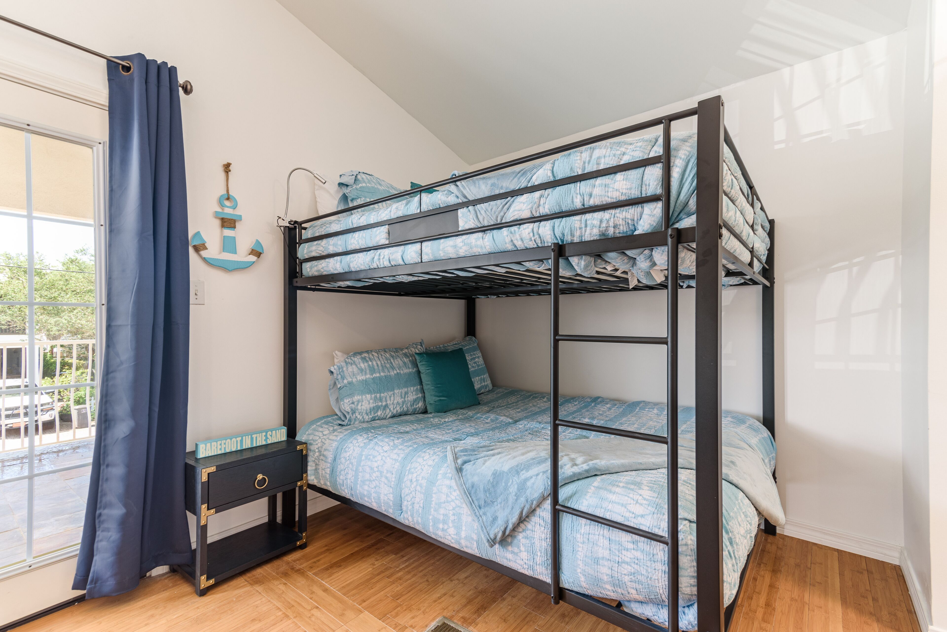 A bunk bed with a blue and white patterned bedspread, a small bedside table with a drawer, and a wall-mounted anchor decoration.