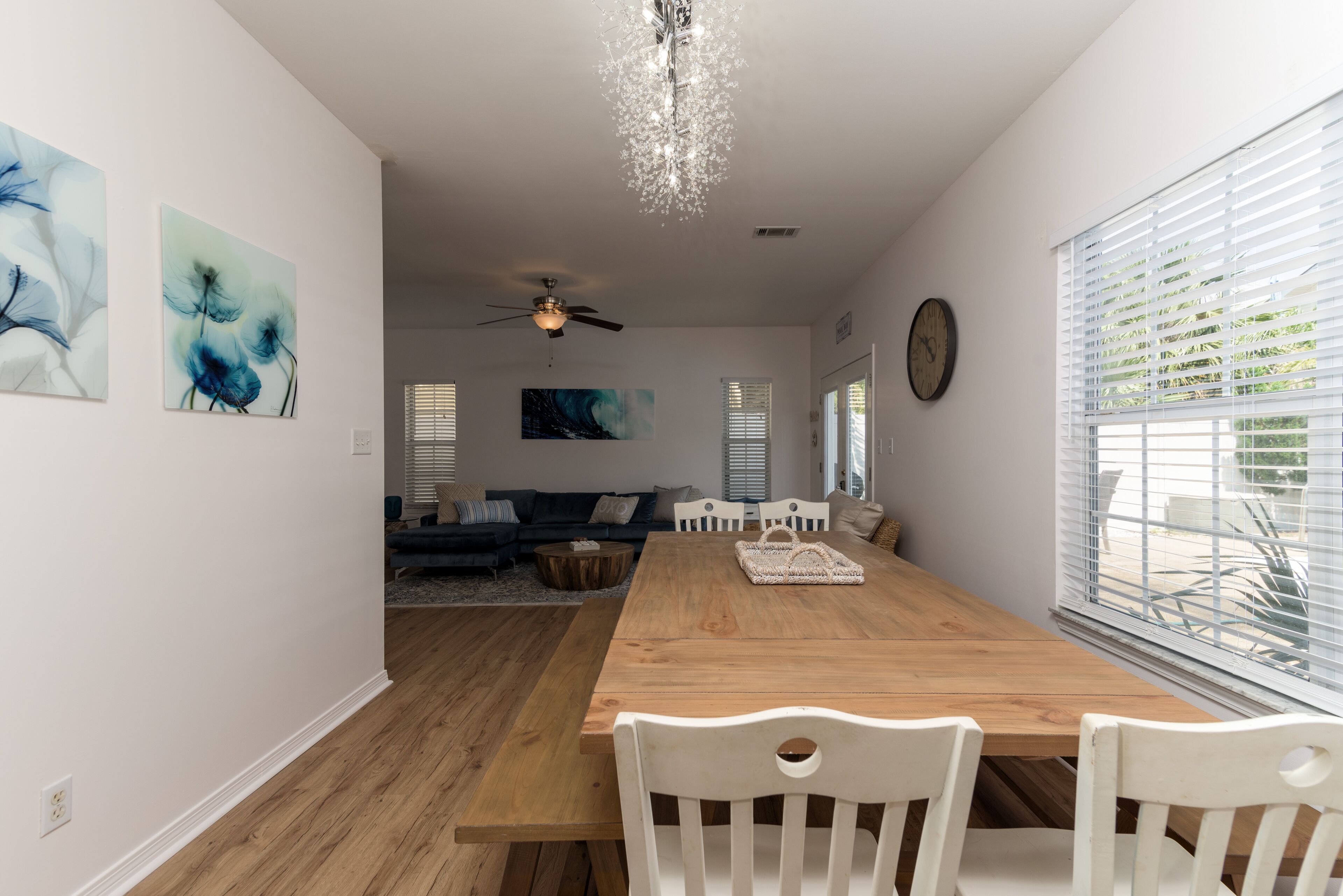Een eetruimte met een houten tafel en witte stoelen, een plafondventilator en kunstwerken aan de muur.