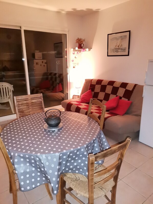 A cozy living room with a dining table, chairs, a sofa, and a refrigerator. - Petit 2 Pièces en Front de mer (Les Sables-d'Olonne)