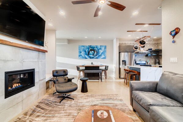 A modern living room with a fireplace, a dining area, and a kitchen.