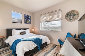 A bedroom with a bed, a desk, a chair, a lamp, and artwork on the walls.