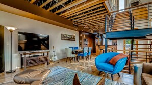 A spacious living room with a large TV, a dining area, and a staircase. - Old Town Loft Oasis with Amazing Rooftop Deck! (Fort Collins)