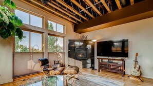 A spacious living room with a fireplace, a large TV, and a guitar. - Old Town Loft Oasis with Amazing Rooftop Deck! (Fort Collins)