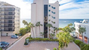 A modern multi-story building with a central glass elevator shaft, surrounded by palm trees and a parking area. - Ocean front , beach views - exquisite sunsets and relaxing setting. (Naples)