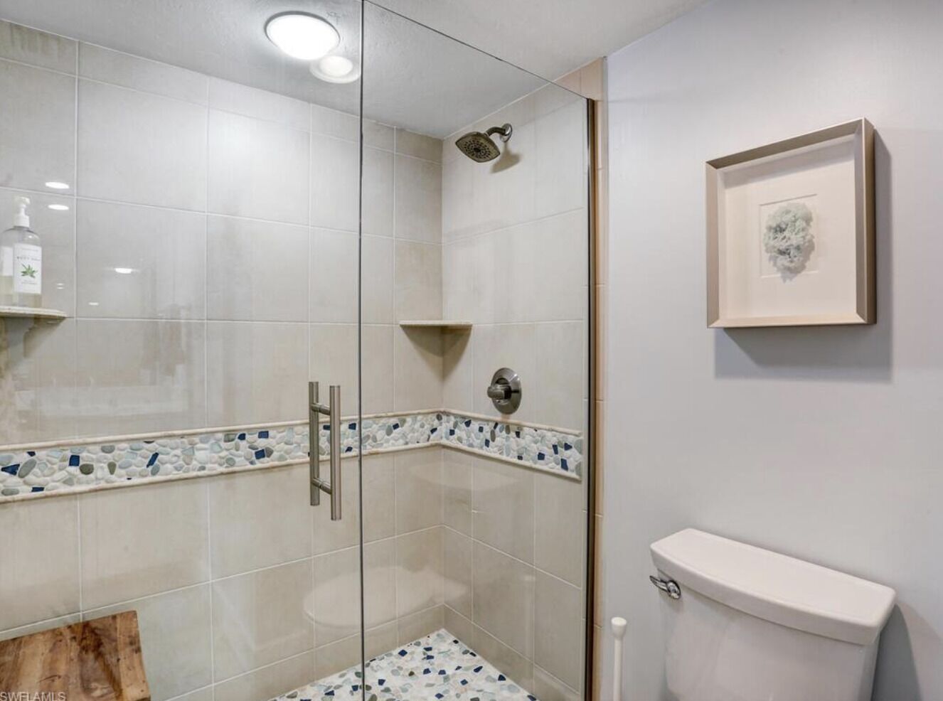 Et moderne badeværelse med et glasvægshus, et hvidt toilet og et billede i ramme på væggen.