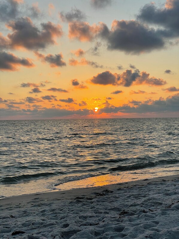 A beach with the sun setting over the horizon, creating a reflection on the water. - Ocean front , beach views - exquisite sunsets and relaxing setting. (Naples)
