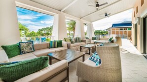 A covered outdoor seating area with sofas, chairs, and a table, overlooking a pool and palm trees. - Luxurious Villa With Modern Decor and Huge Pool in Upscale Resort! #6s820 (Kissimmee)