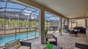 A covered patio area with a pool, outdoor furniture, and a view of a greenhouse structure. - Luxurious Villa With Modern Decor and Huge Pool in Upscale Resort! #6s820 (Kissimmee)