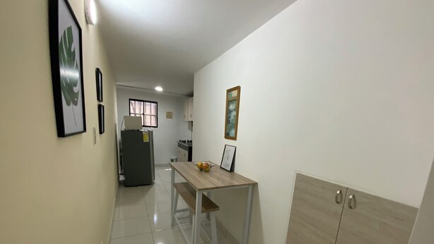 A narrow hallway with a kitchen area featuring a refrigerator, a dining table with chairs, and a cabinet with drawers. - Cute 1 room apartment Laureles (Medellín)