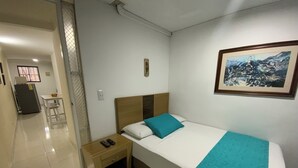A hotel room with a bed, a nightstand, a small table, and a chair. There is a painting on the wall and a window in the background. - Cute 1 room apartment Laureles (Medellín)