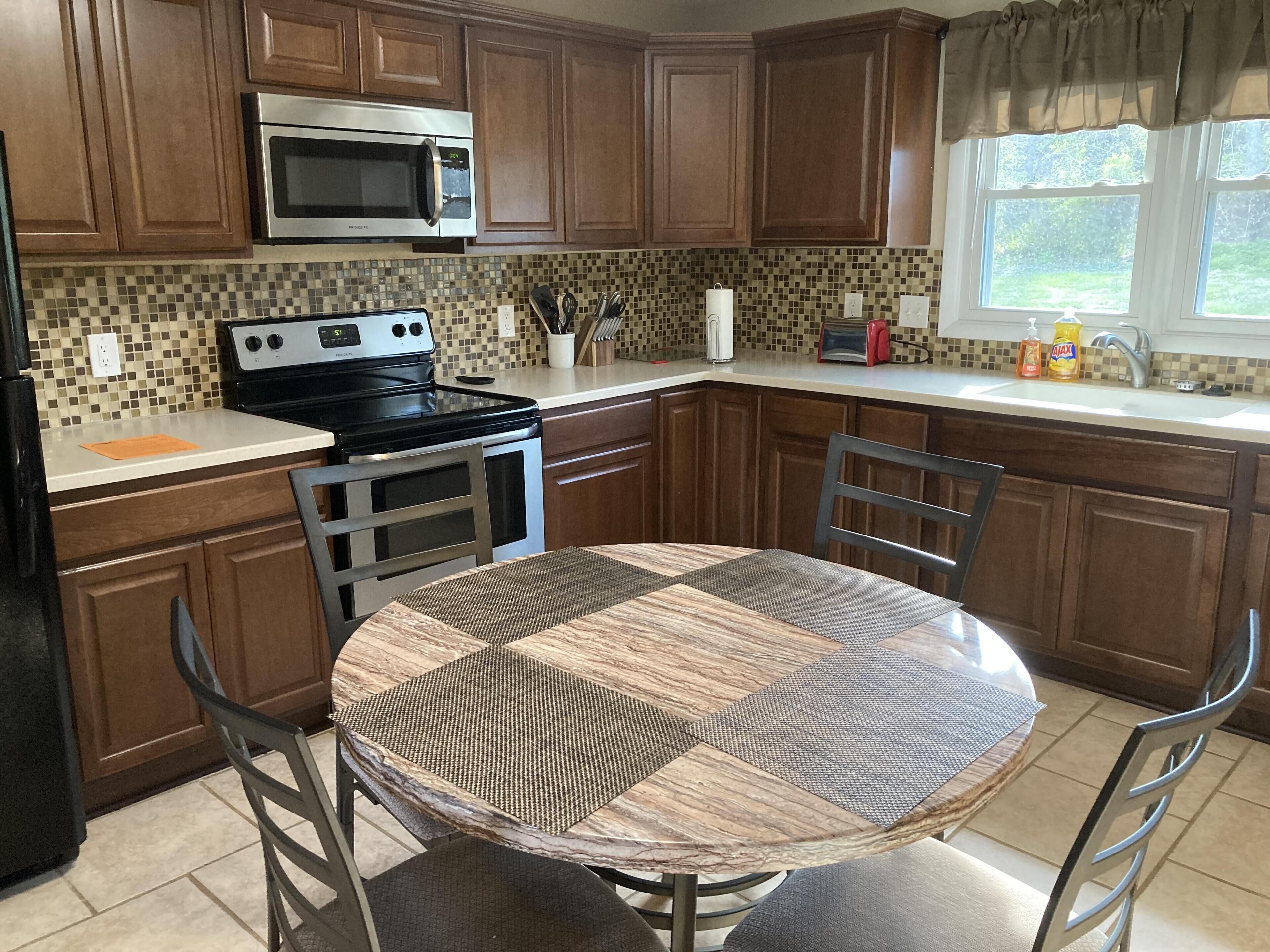 A kitchen with wooden cabinets, a stainless steel microwave, a stove, and a dining table with chairs.