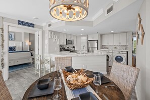 A modern kitchen with stainless steel appliances, a dining area with a round table, and a view of the beach. - Ocean Views at Villamare 1405 in Palmetto Dunes, Steps to the Beach! (Hilton Head Island)