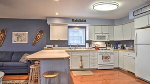 A compact kitchen with white cabinets, a central island with stools, a microwave, and a refrigerator. - Downtown Boyne City Home, Walk to Lake Charlevoix! (Boyne City)