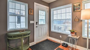 A hallway with a door, two windows with blinds, a small table with a plant, and a rug. - Downtown Boyne City Home, Walk to Lake Charlevoix! (Boyne City)