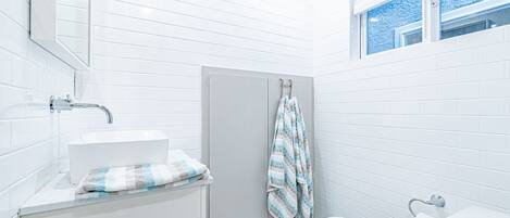 A small, modern bathroom with white tiles, a white sink, a toilet, and a shower area.